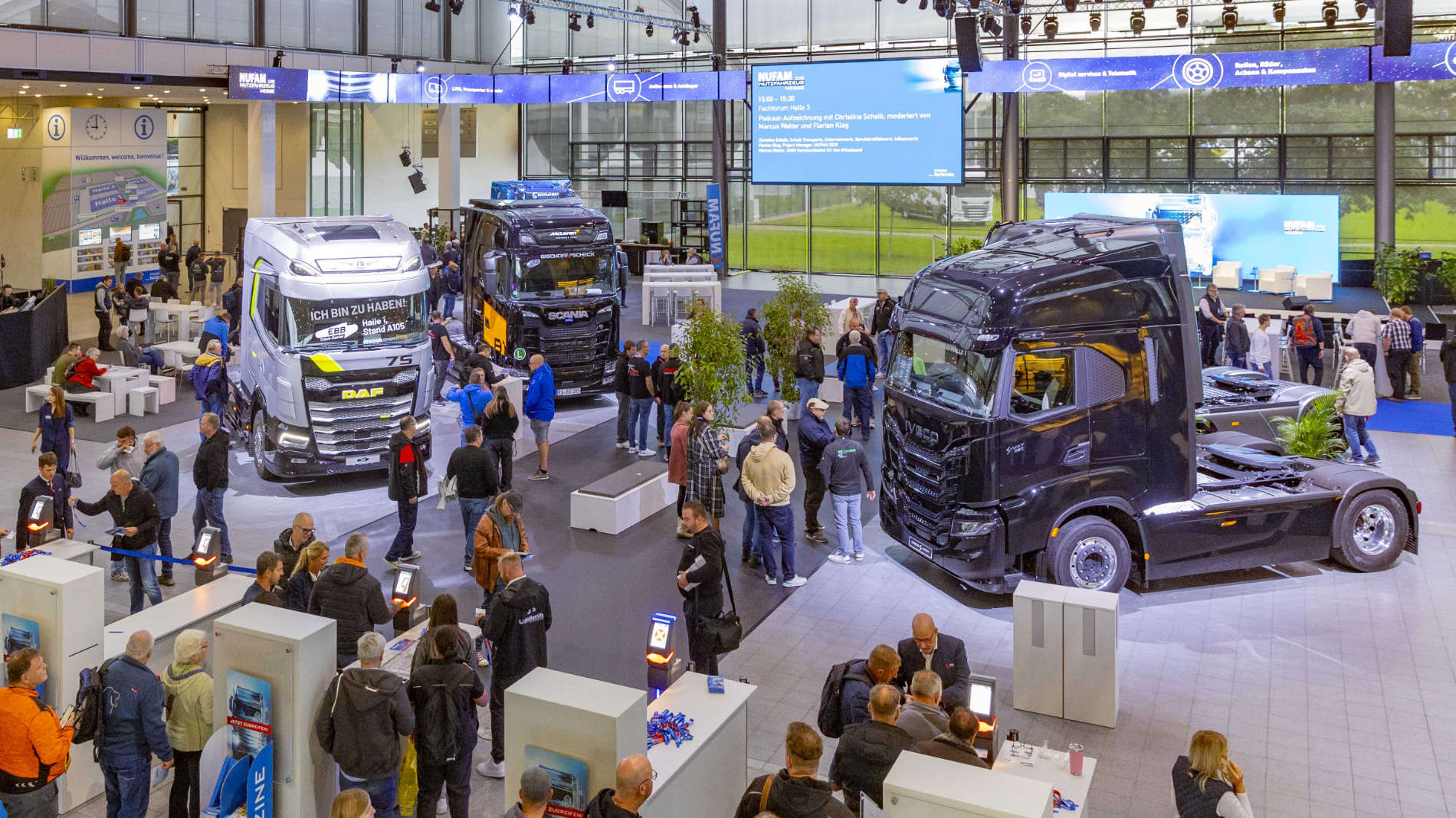 Overview of the exhibition hall with DAF, Iveco and Scania trucks and numerous visitors.
