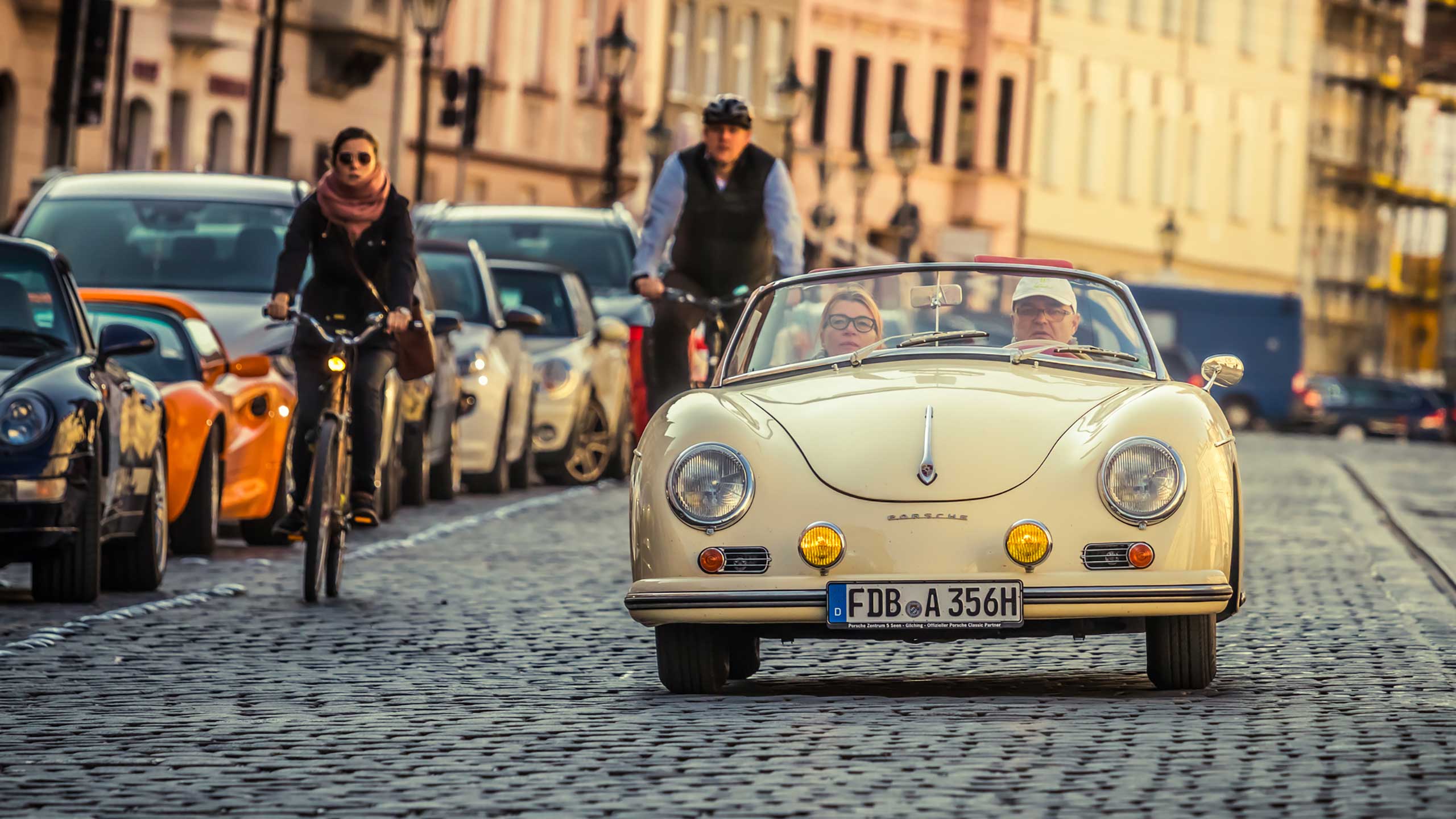 Klassischer cremefarbener Porsche-Cabrio fährt über eine gepflasterte Straße in der Stadt.