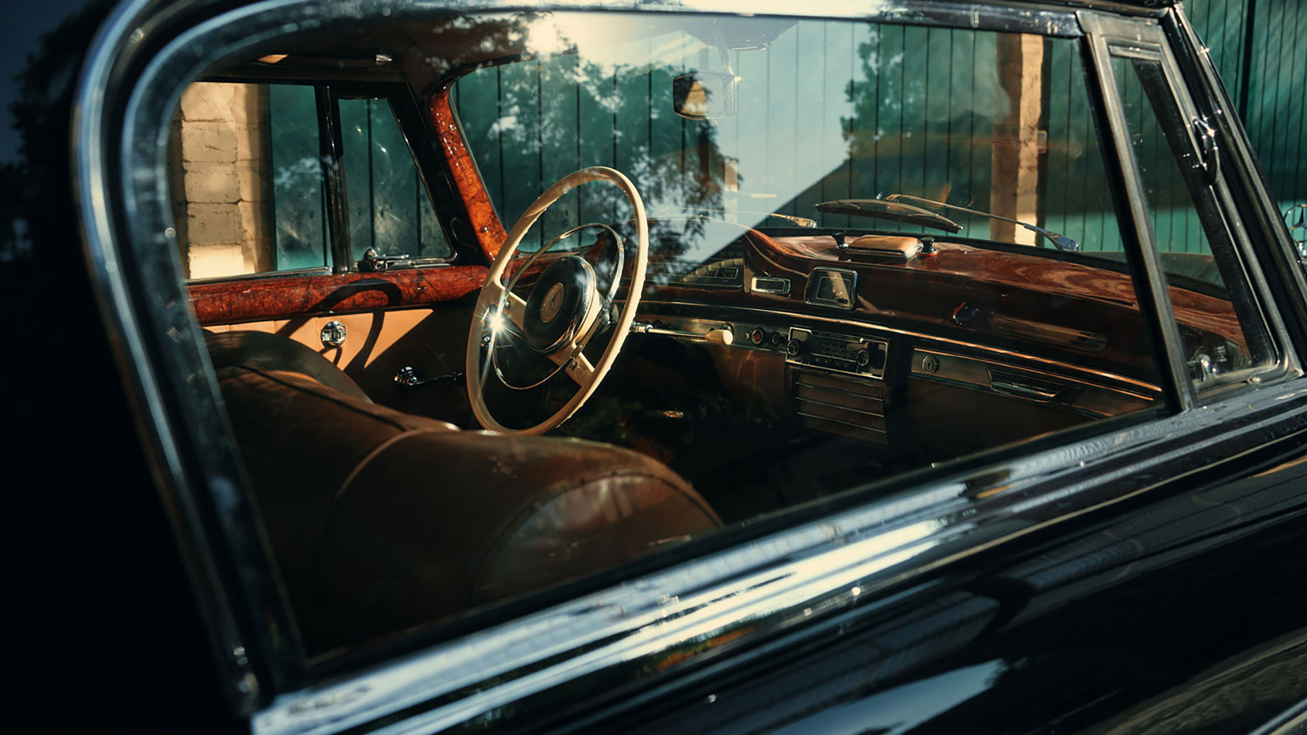 Blick durch das Seitenfenster auf den Innenraum eines klassischen Autos mit Holzarmaturenbrett, Lenkrad und Ledersitzen.