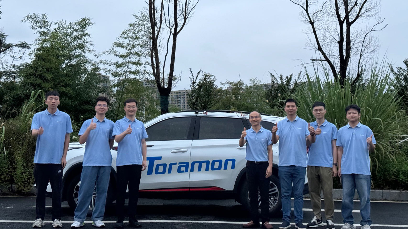 Toramon team in front of a car with company lettering