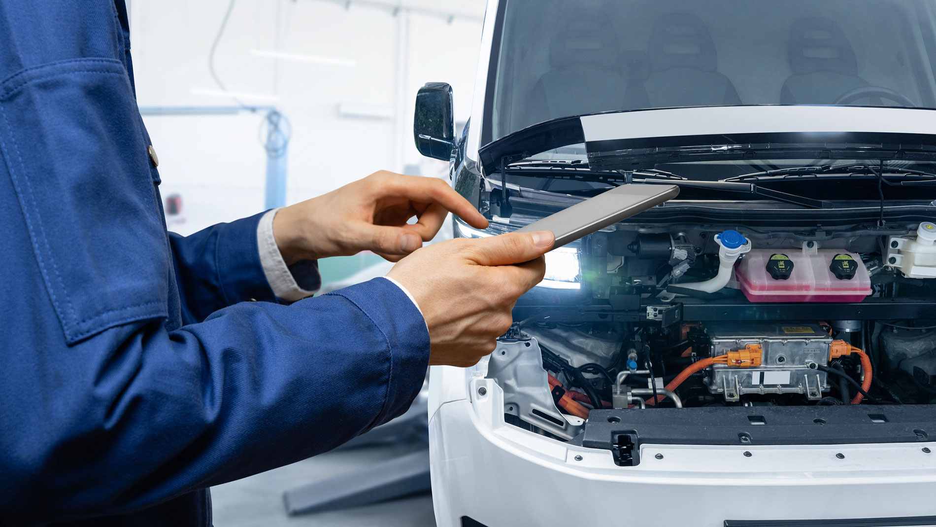Automotive technician inspecting an electric vehicle using a tablet in a modern workshop.