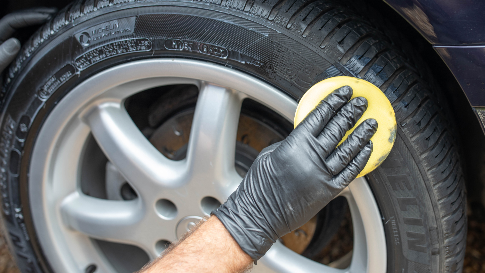 A hand rubs a sponge over a car tyre.