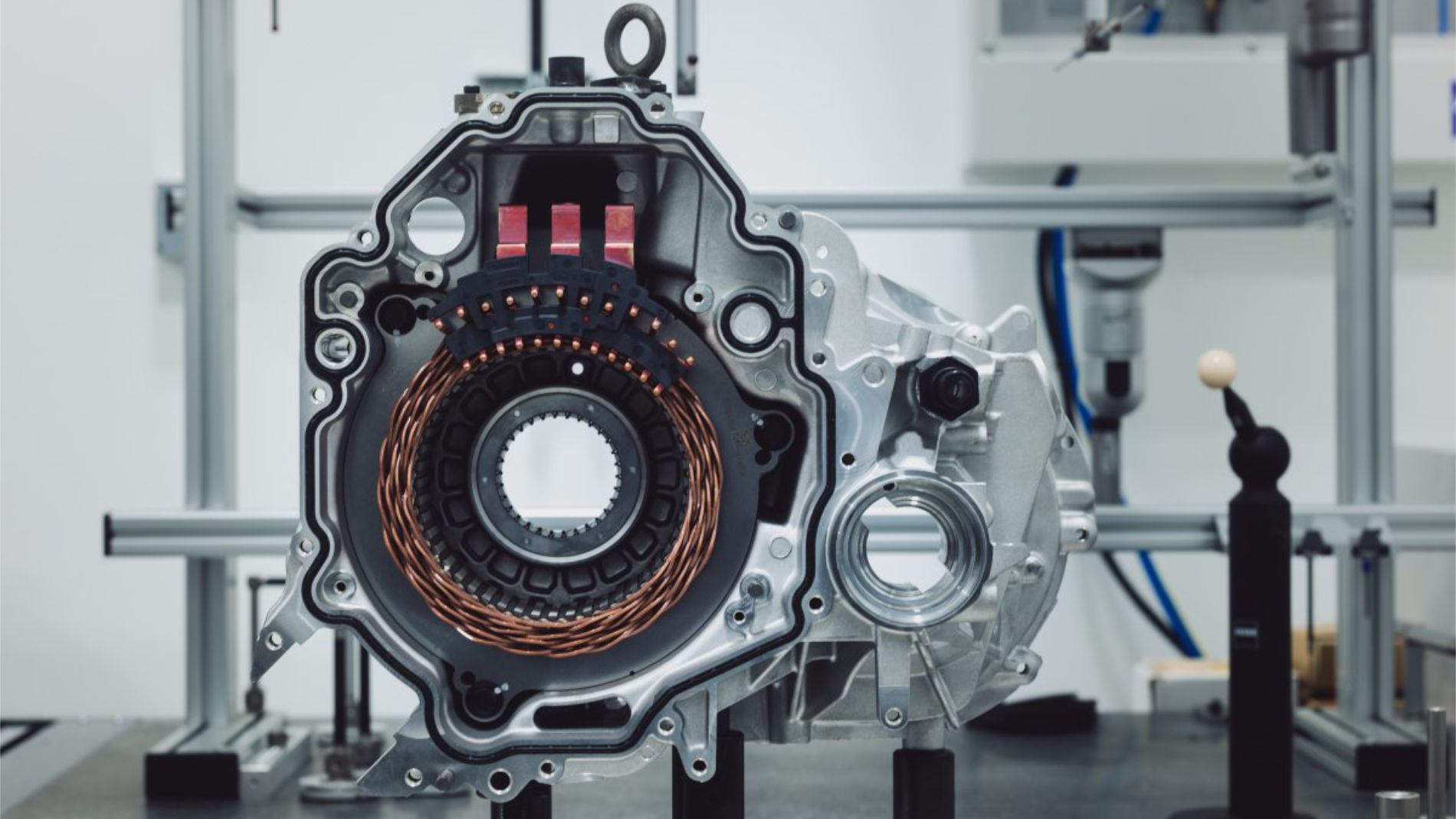 Open casing of an electric motor with visible copper coils, on a test bench in a workshop.