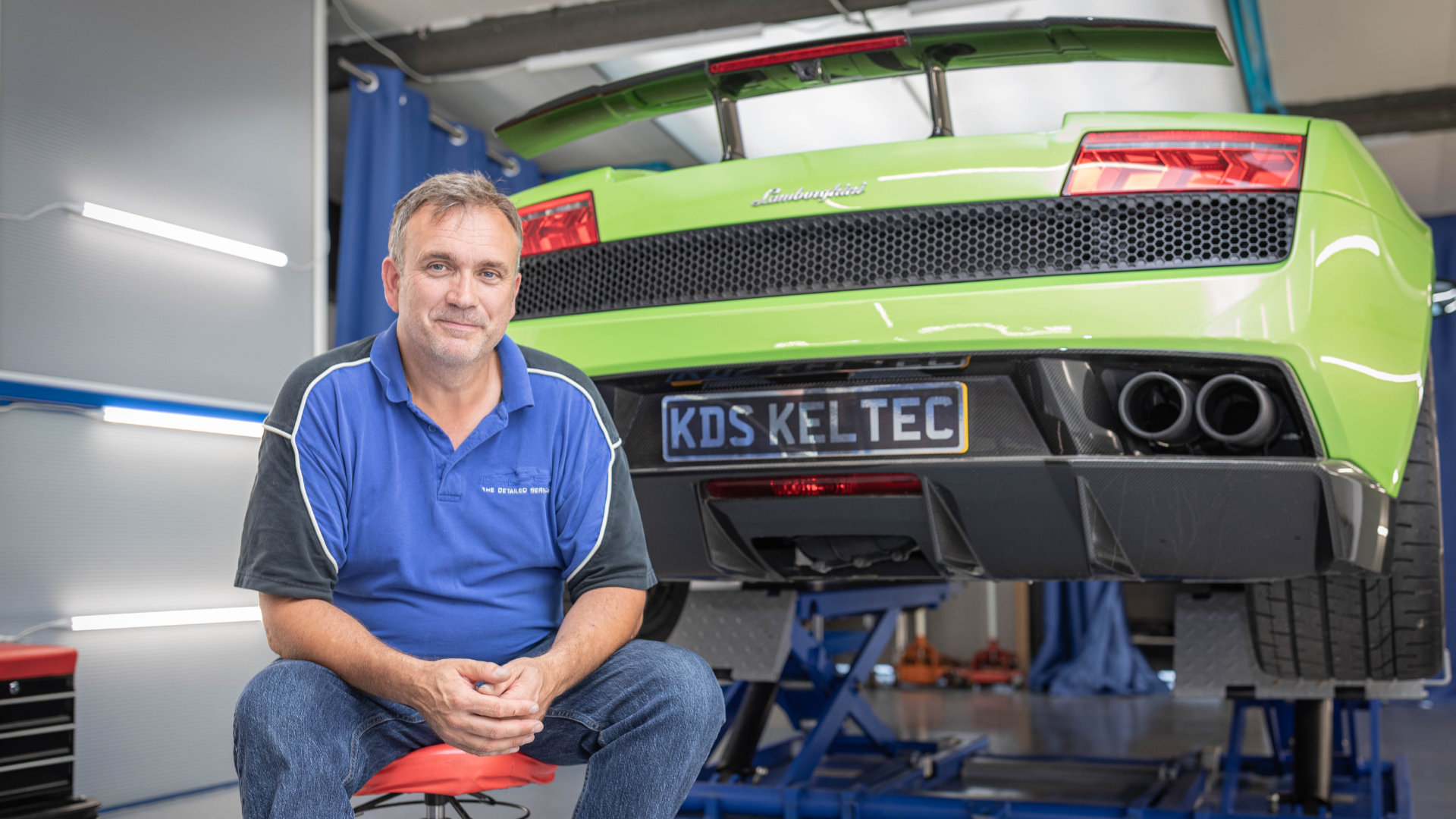 Mann sitzt vor einem grünen Auto auf einer Hebebühne