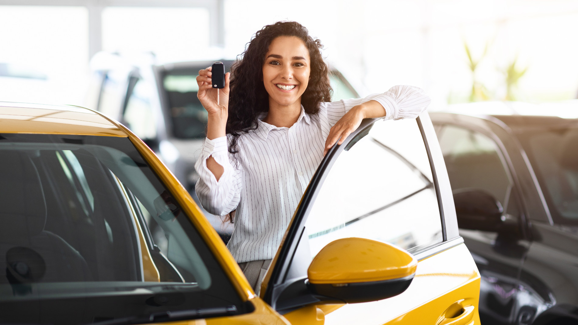 Woman presenting car key beside yellow car