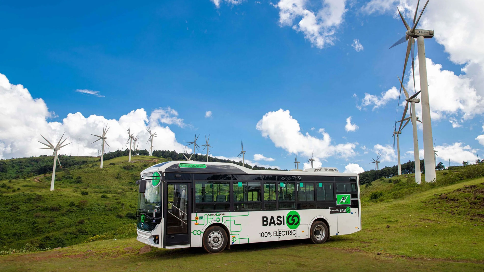 Electric bus in front of wind turbines in green hilly landscape