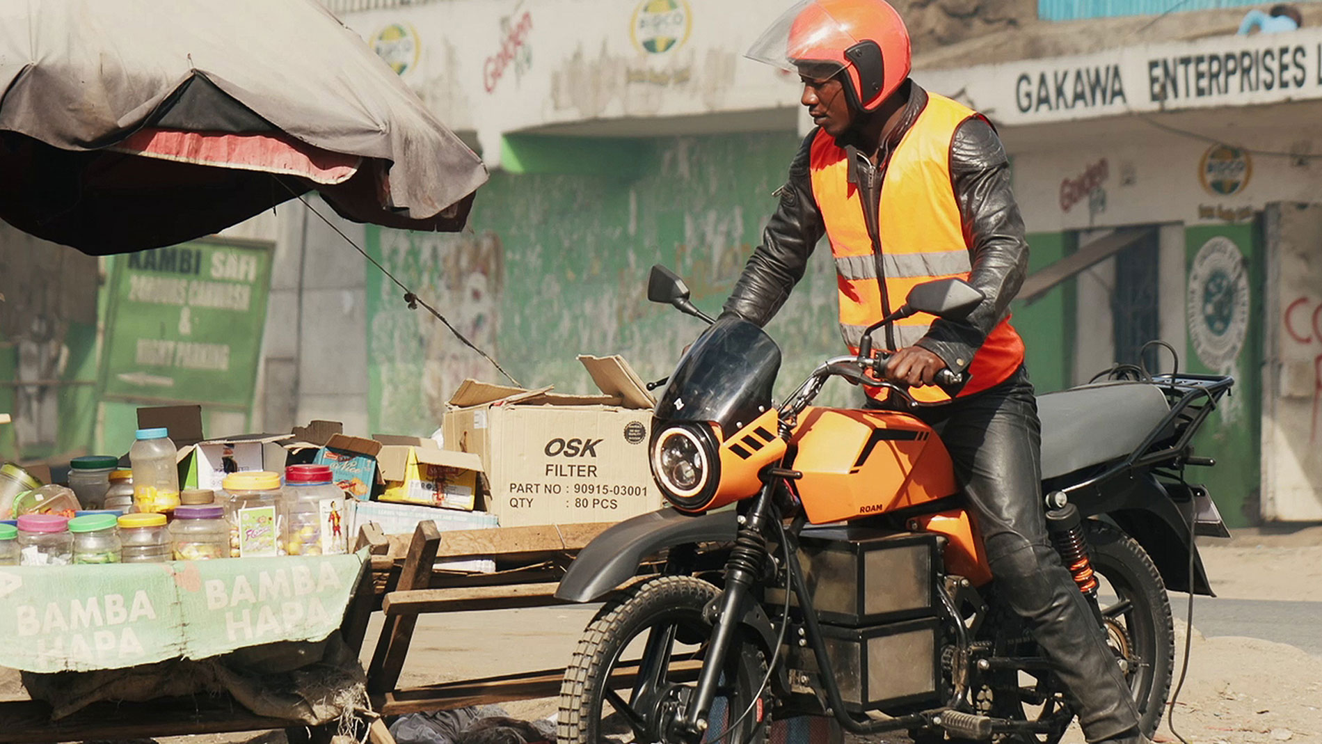 Motorbike rider in safety vest on electric delivery motorcycle at street market in East Africa
