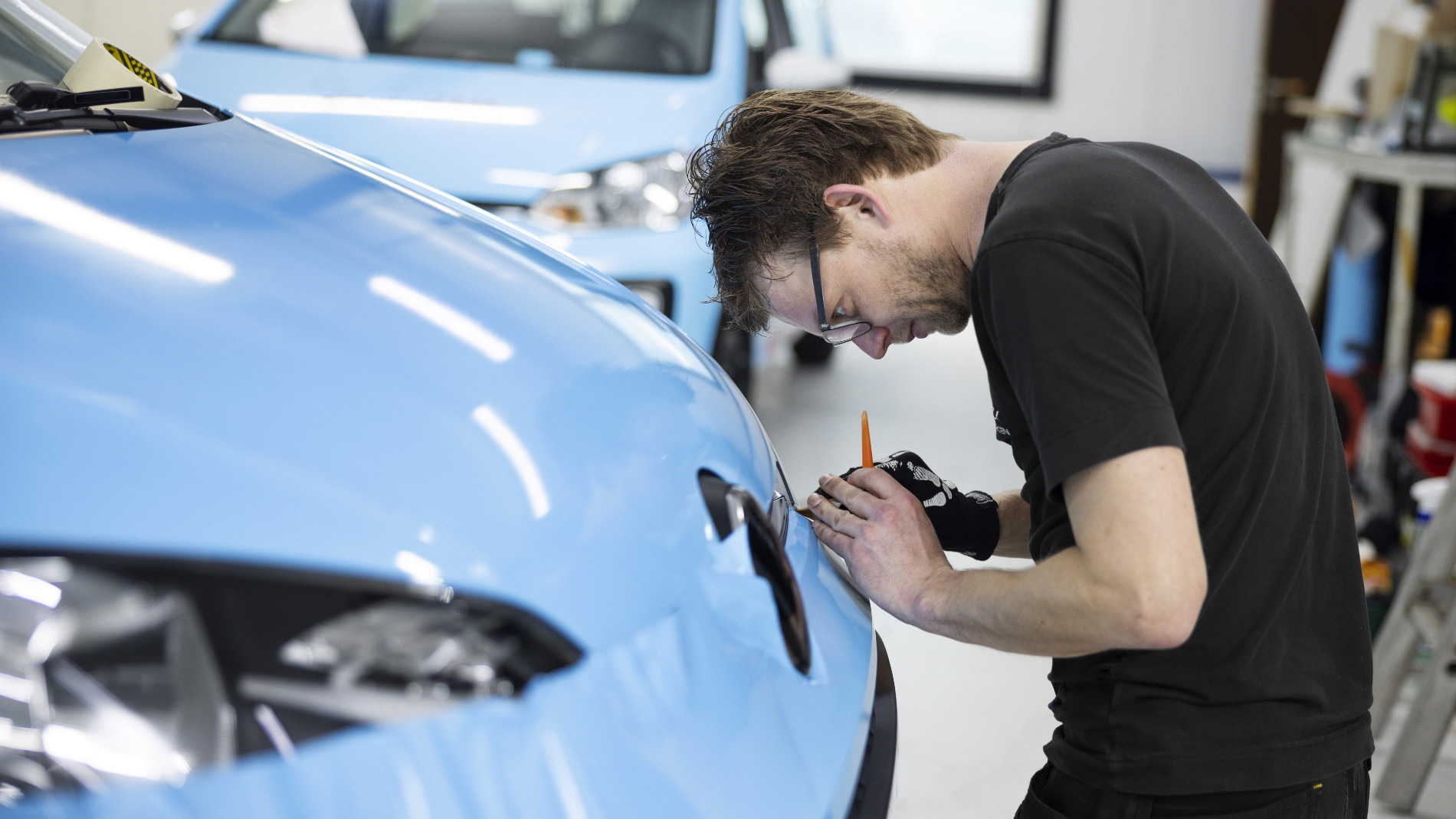 A man is repairing the bodywork of a blue car in a garage
