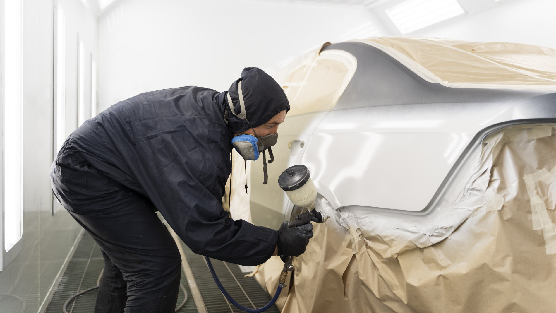 A person is painting a car with a spray gun in a paint booth