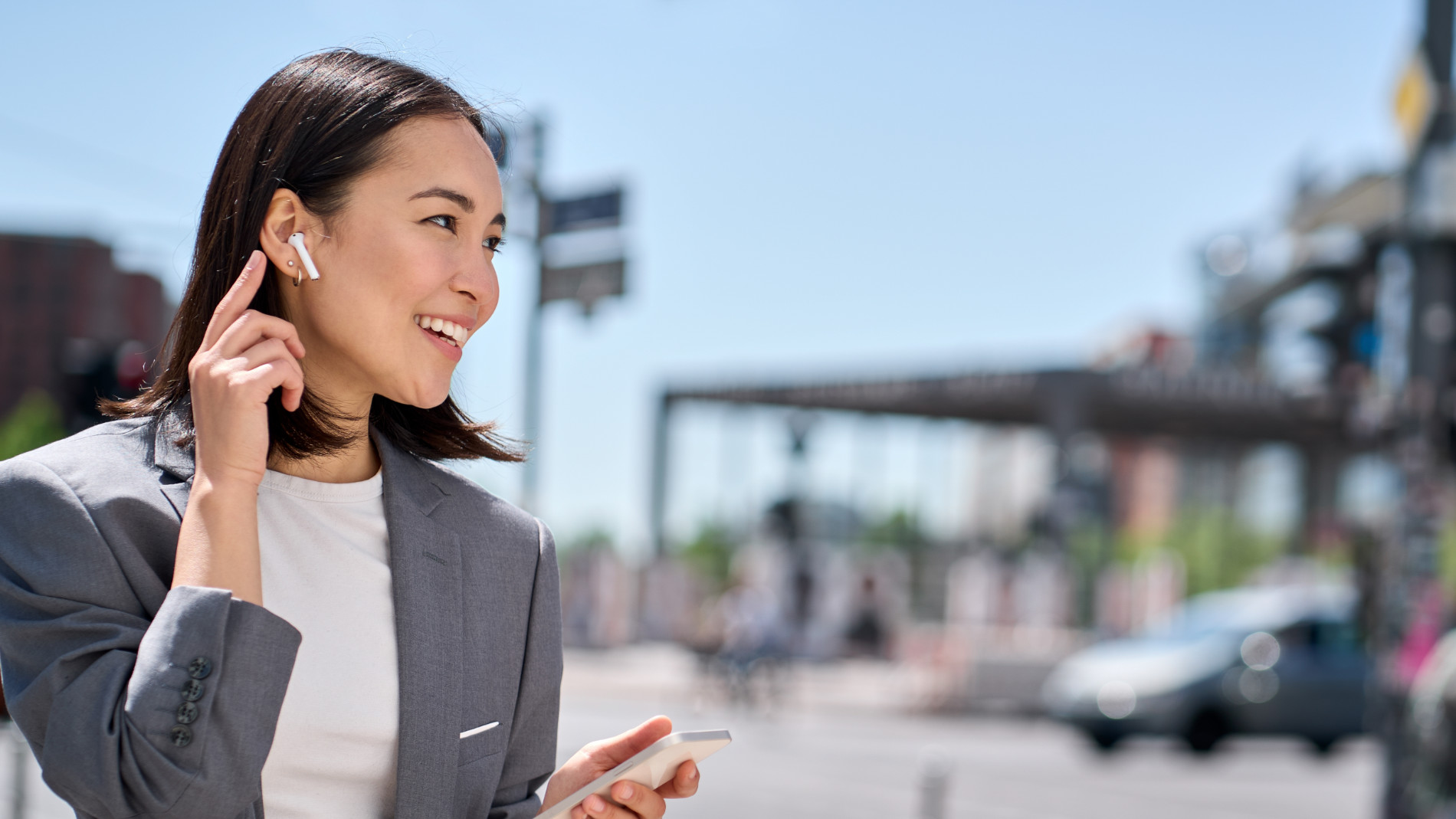 Woman in business attire talking with wireless earbuds on a sunny street